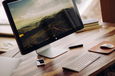 白天，在棕色木制电脑桌上的魔法键盘旁放置灰色iMac